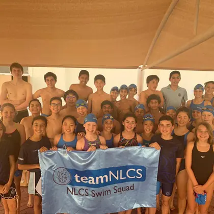 The senior swim squad with a team banner at the pool