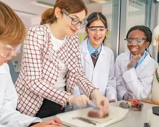 Students in white lab coats gather round a skeleton model with their teacher in a science laboratory